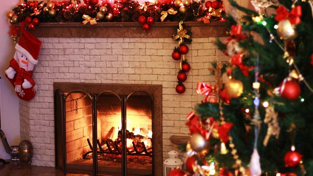 A cozy fireplace with holiday decorations and a Christmas tree on display.